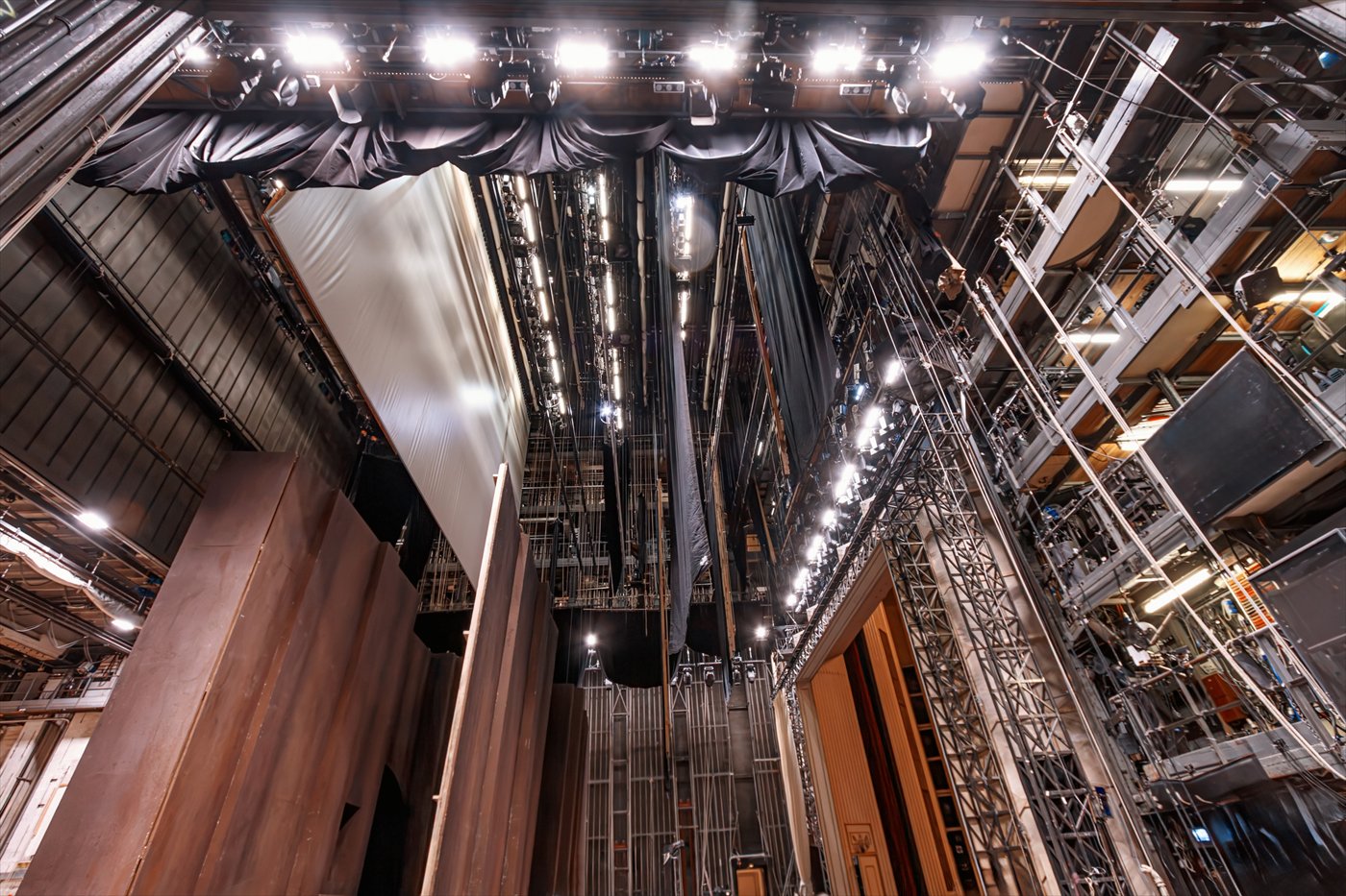 A view straight up into a working fly system, hanging soft goods and scenic pieces caught mid-air.